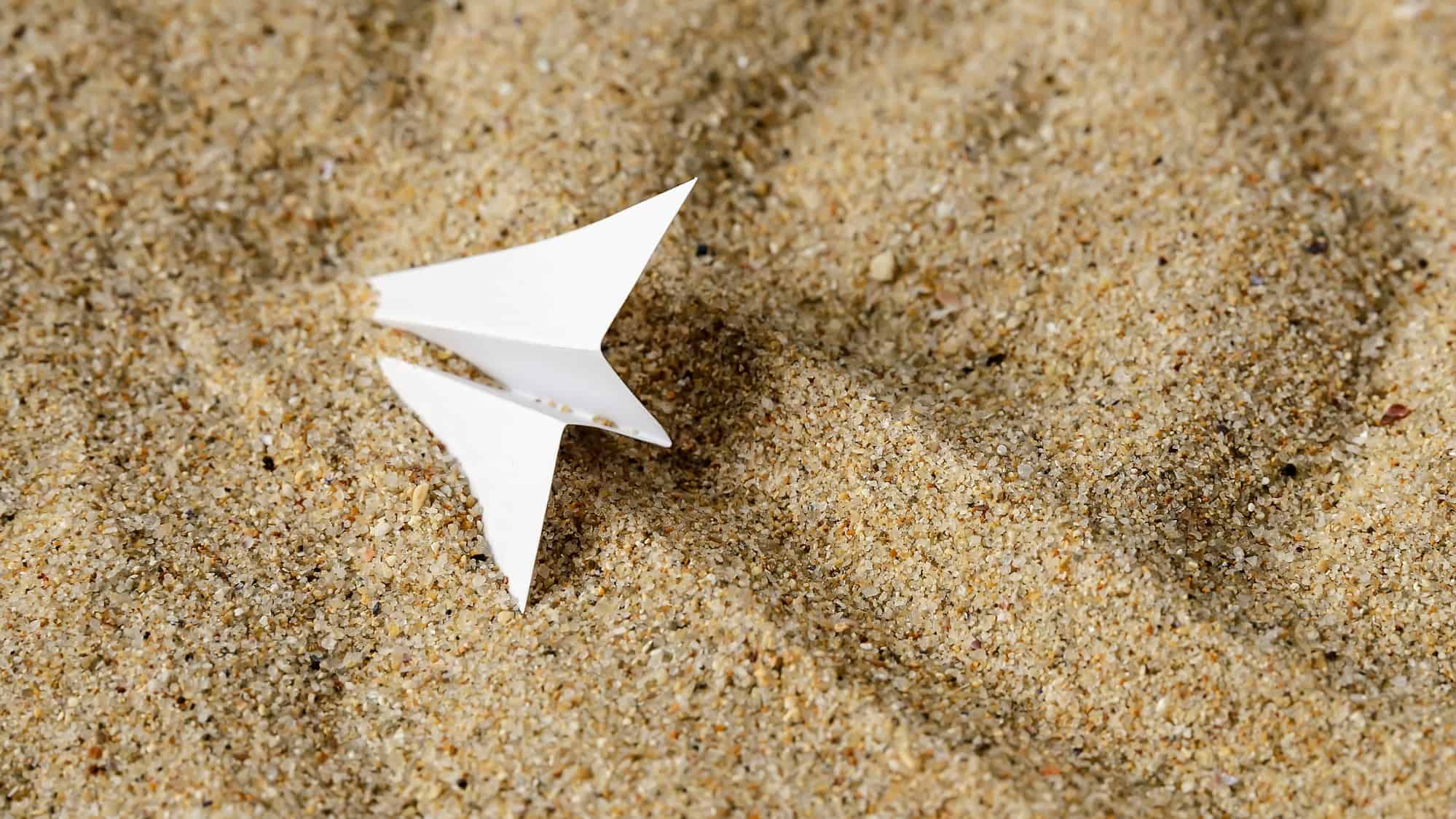 A paper plane crashed in sand.