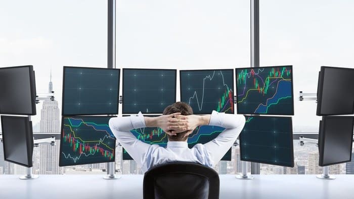 Investor sits in front of multiple screens and watches stock prices