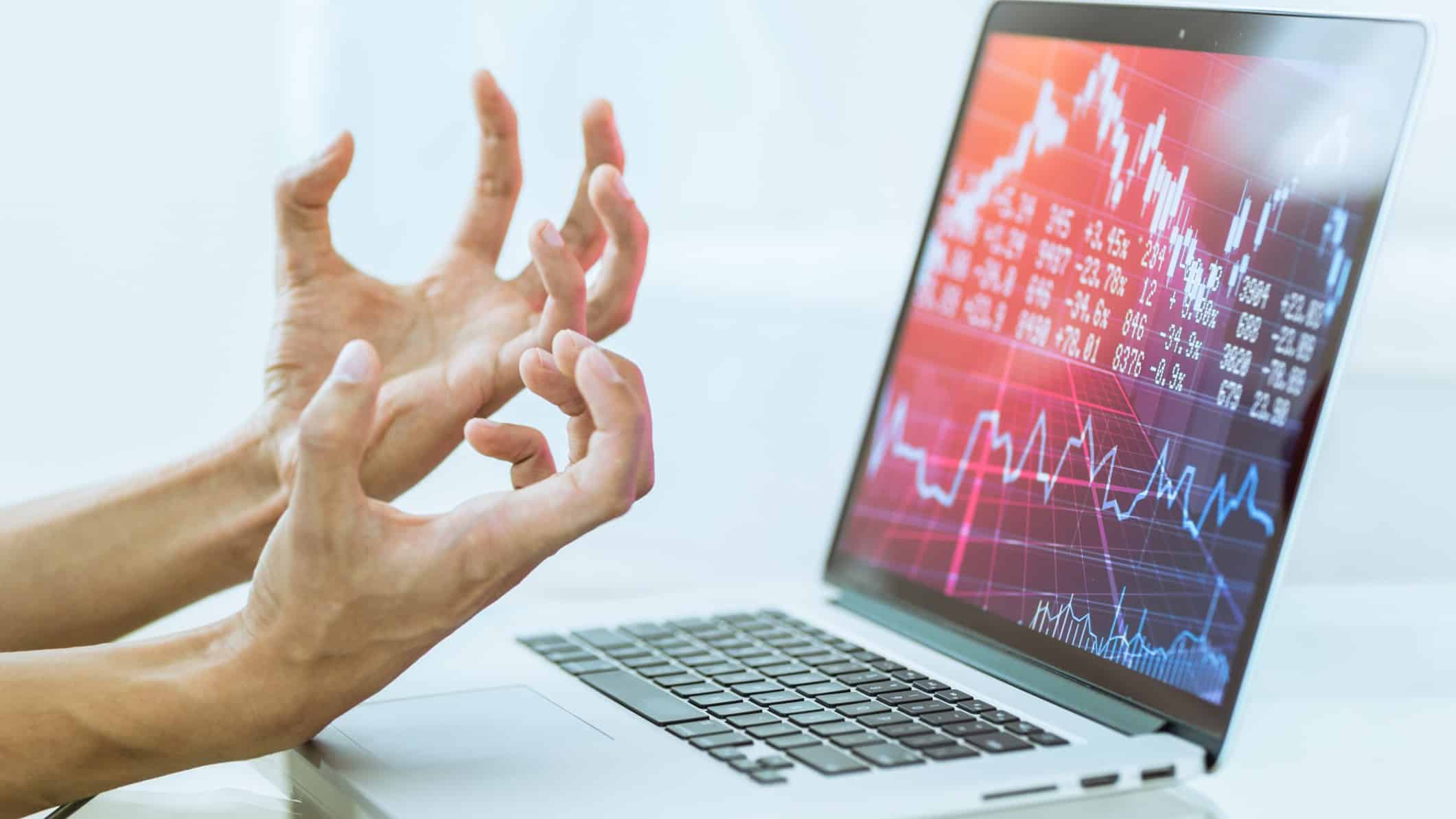 hands making frustrated gesture at computer screen depicting stock market crash charts