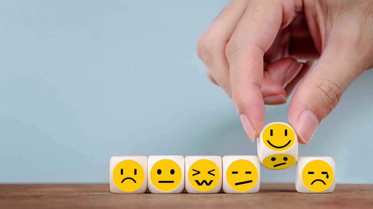 hand picking dice with happy face from selection of neutral and sad face dice