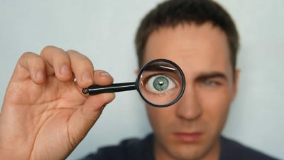 close up of man's eye looking through magnifying glass representing asx 200 share price on watch