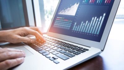 hand restin g on laptop computer keyboard with stock prices on screen