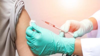 gloved hand injecting coronavirus vaccine into person's arm