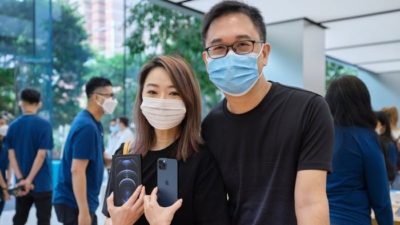 Man and woman in blue face masks hold up Apple iPhones in an Apple store