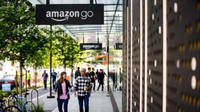 amazon stock represented by people walking along shopping strip under Amazon Go sign