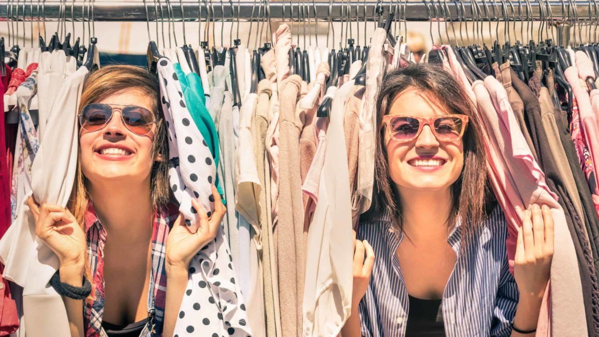 Two happy shoppers finding bargains amongst clothes on a store rack