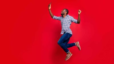 rising ASX Telstra share price represented by man jumping in the air for joy looking at mobile phone