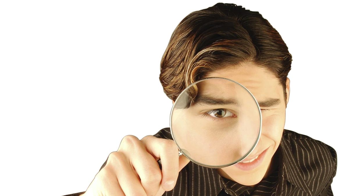 asx share price on watch represented by young man looking intently through magnifying glass