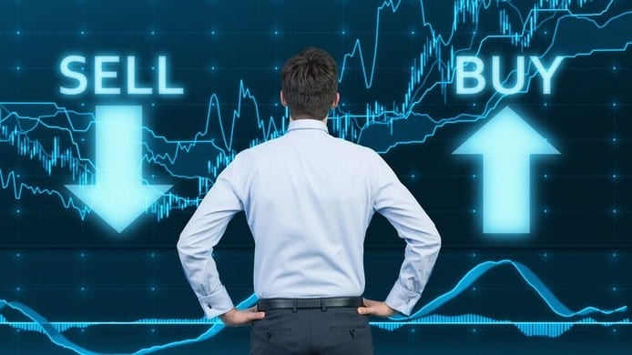 Businessman with hands on hips looks at share price chart with the words 'buy' and 'sell '