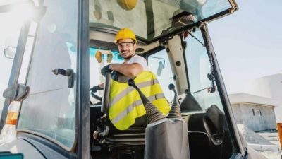 male wearing high vis vest smiling while sitting in excavator cabin