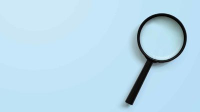 Magnifying glass on blue background symbolising searching for ASX shares