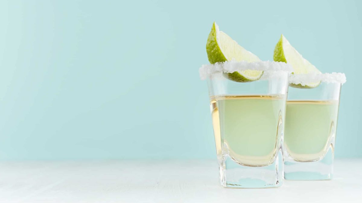 Two shot glasses with tequila, salt and lime on a light blue background