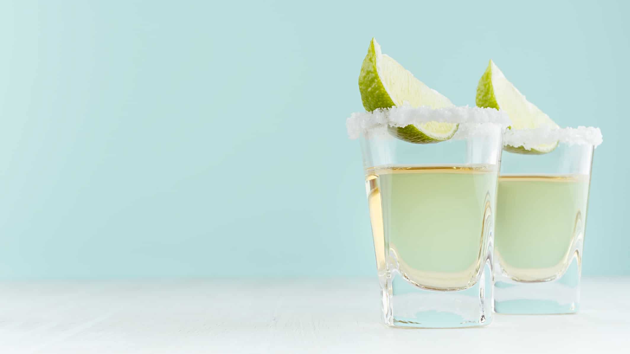 Two shot glasses with tequila, salt and lime on a light blue background