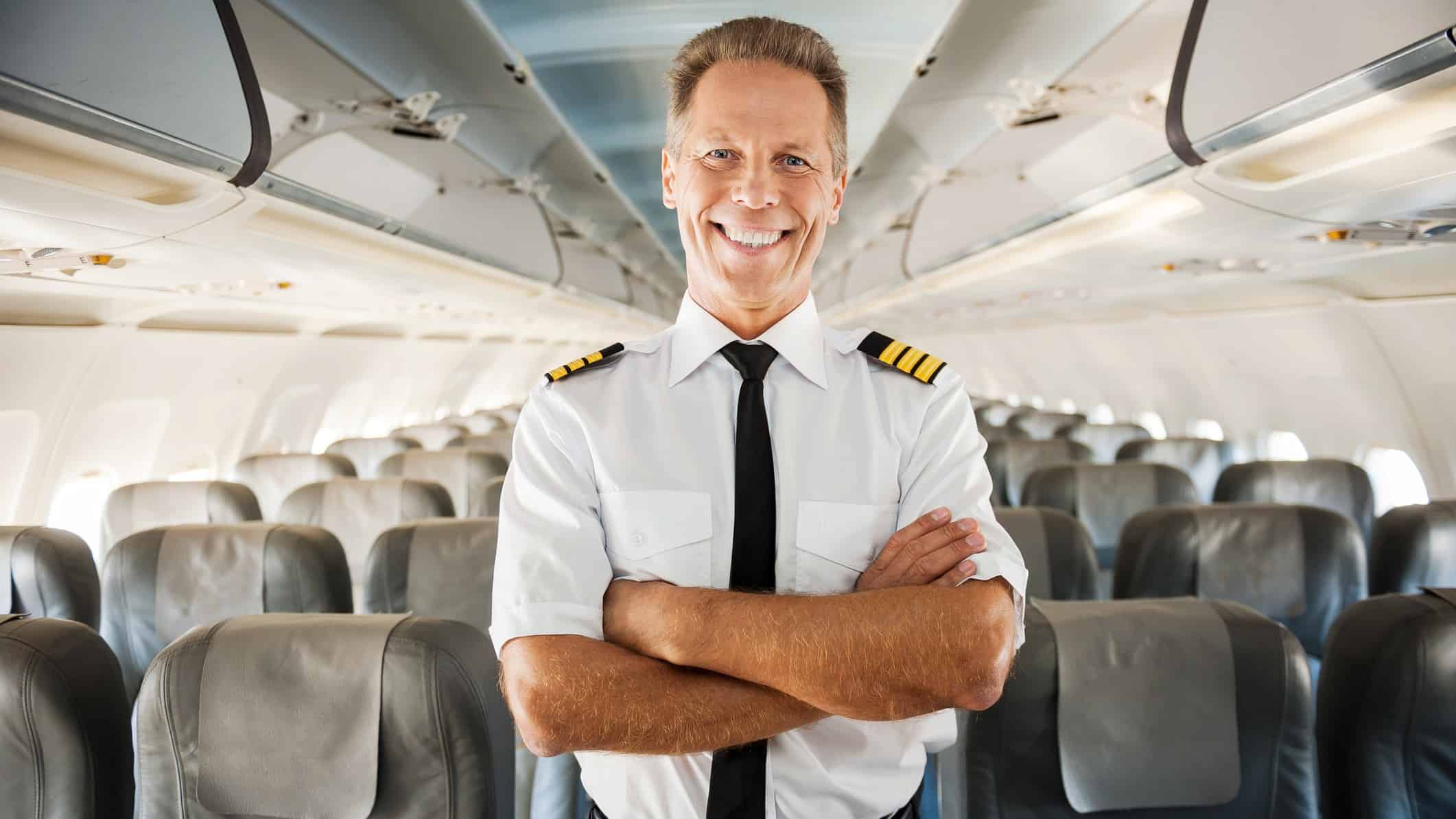 A Qantas pilot stands in an empty passenger cabin smiling with his arms crossed feeling excited about international travel resuming
