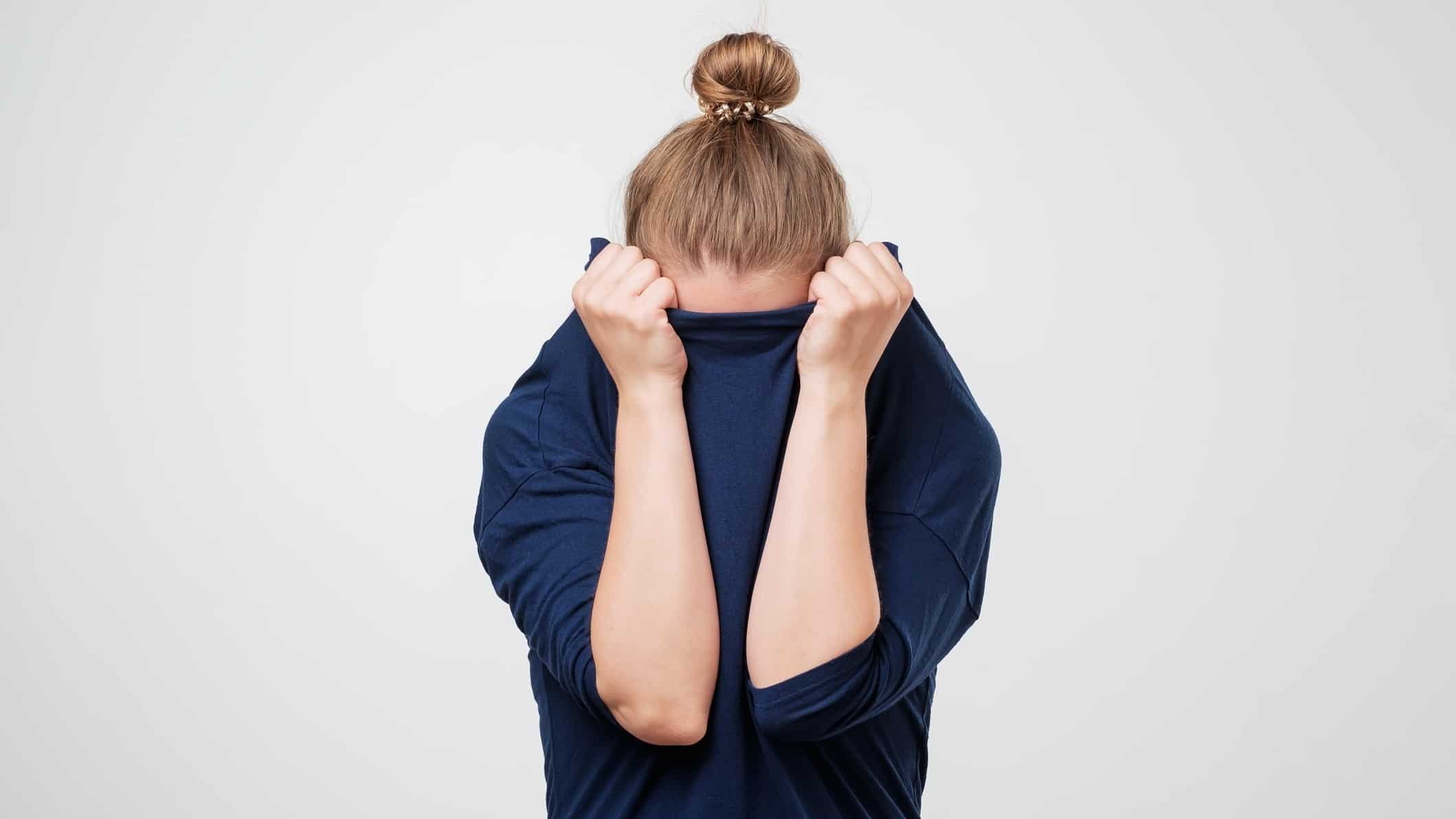 Bad asx shares broker downgrade represented by woman hiding face under her jumper.
