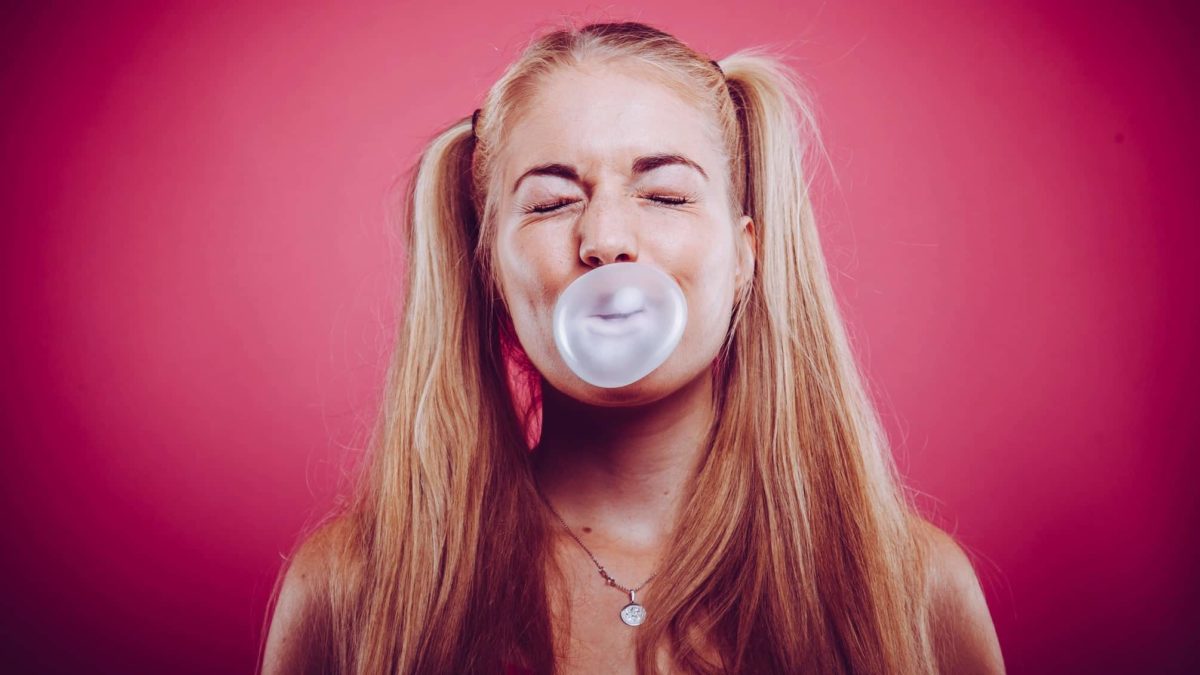 A young woman in pigtails blowing bubblegum against a red background