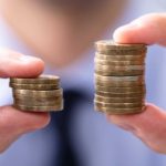 man holding two stacks of coins varying in size representing a comparison of dividend yields between Medibank and NIB