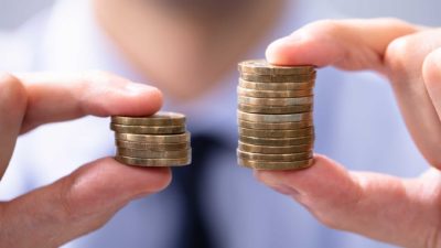 man holding two stacks of coins varying in size representing a comparison of dividend yields between Medibank and NIB