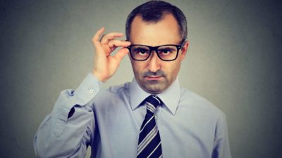 Unimpressed businessman looks down his glasses, indicating an unhappy and critical investor