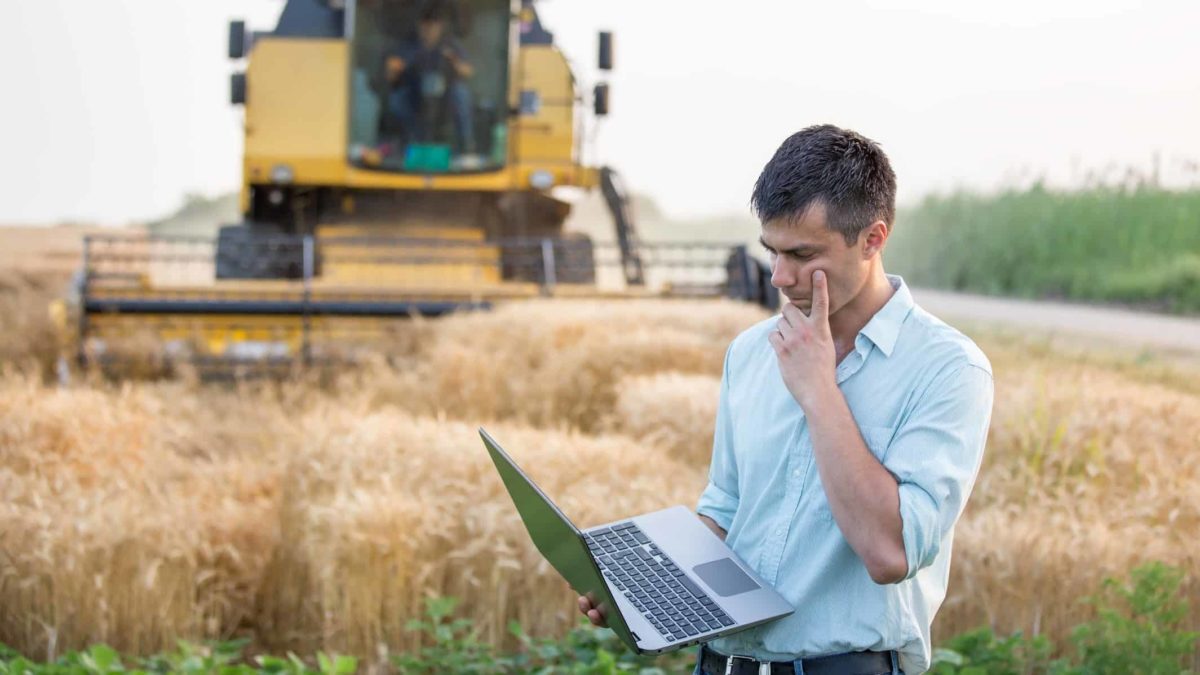 worried famer looks at his computer in front of a harvester, indicating poor prices on the share market