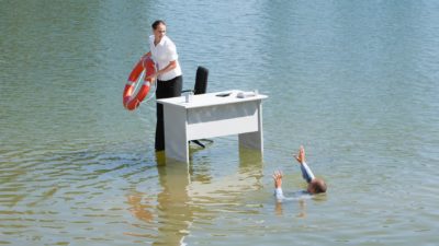 Businessman standing on a desk throwing a lifelife to another sinking in water indicating jobs rescue