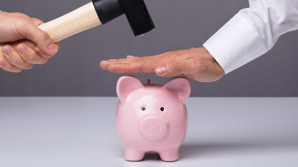 A hand protecting a pink piggy bank from being smashed by a hammer, representing the prevention of bank or government raids on super