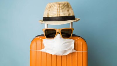 travel asx share price represented by suitcase wearing covid mask