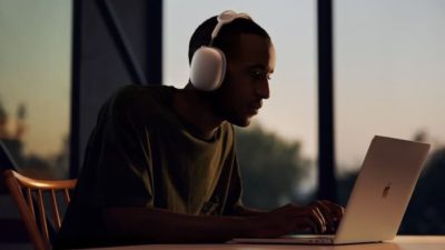 Man with headphones sits over an Apple laptop