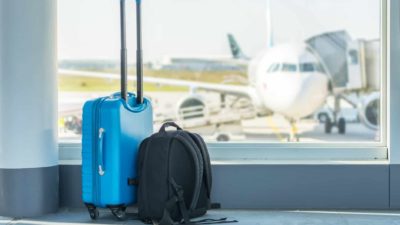 Travel bags sit by an airport lounge window overlooking a grounded plane on the tarmac