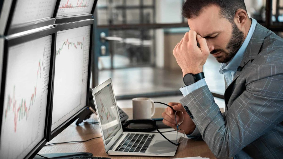 A businessman in front of a computer with his head on his hand in disbelief, indicating poor IPO or share price performance