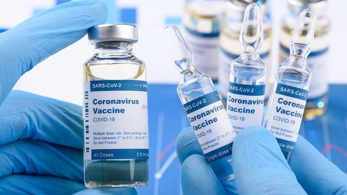Hand with blue medical gloves holds vials of coronavirus vaccines