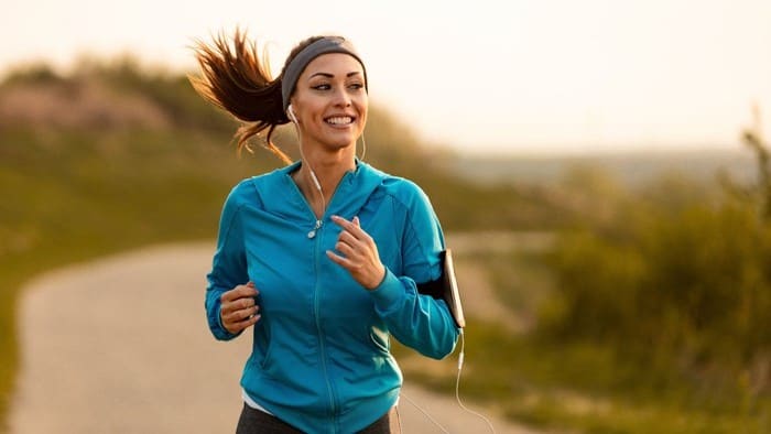 A female dressed in sports gear smiles as she runs along a road, indicating a positive share price for sports apparel companies