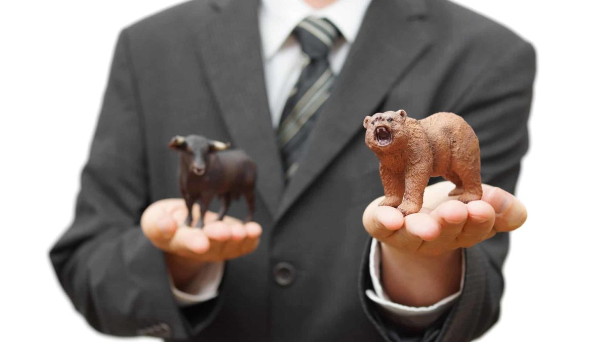 Businessman holding bear figurine in one palm and bull figurine in other