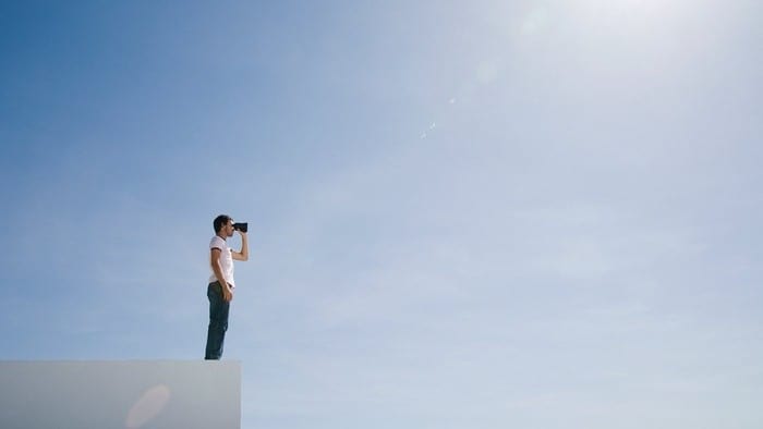 Man with binoculars standing on edge of building looking into distance