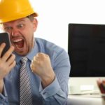 Happy man with a mining hat pumping his fist, on a mobile phone.