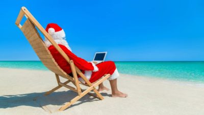 Santa sitting on beach looking up best ASX shares to buy on a laptop.
