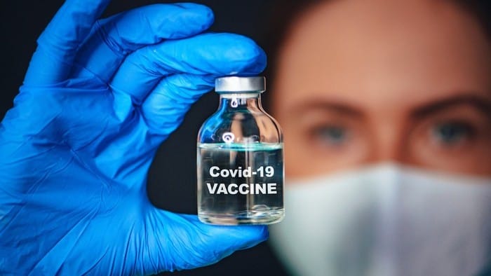 woman waering face mask holding vial of covid-19 vaccine