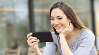 Woman sitting and looking at her phone smiling watching the share price go up