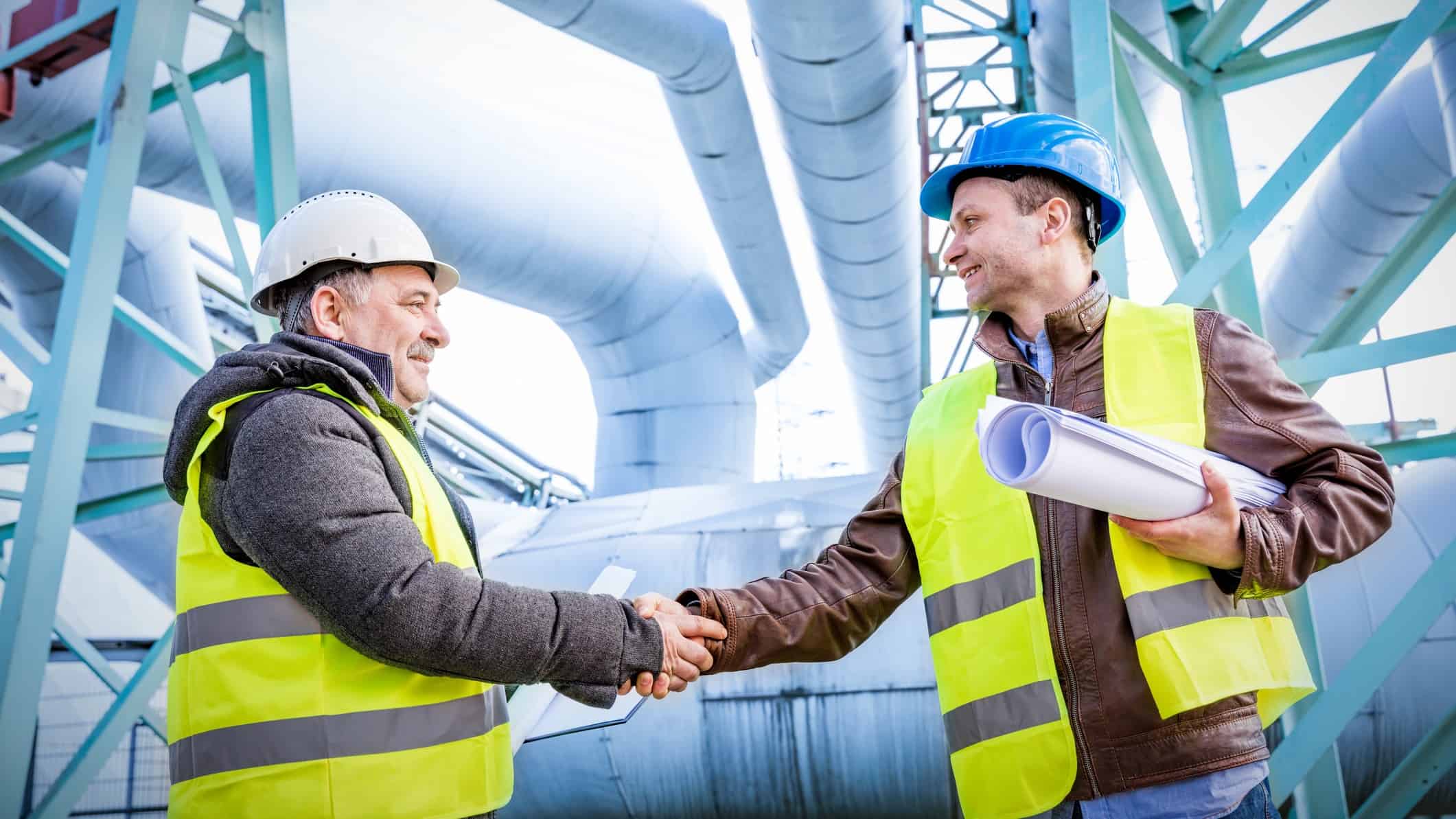 two men in mining hats shake hands on a deal with gas pipelines in the background, indicating a deal between Senex and 29 Metals