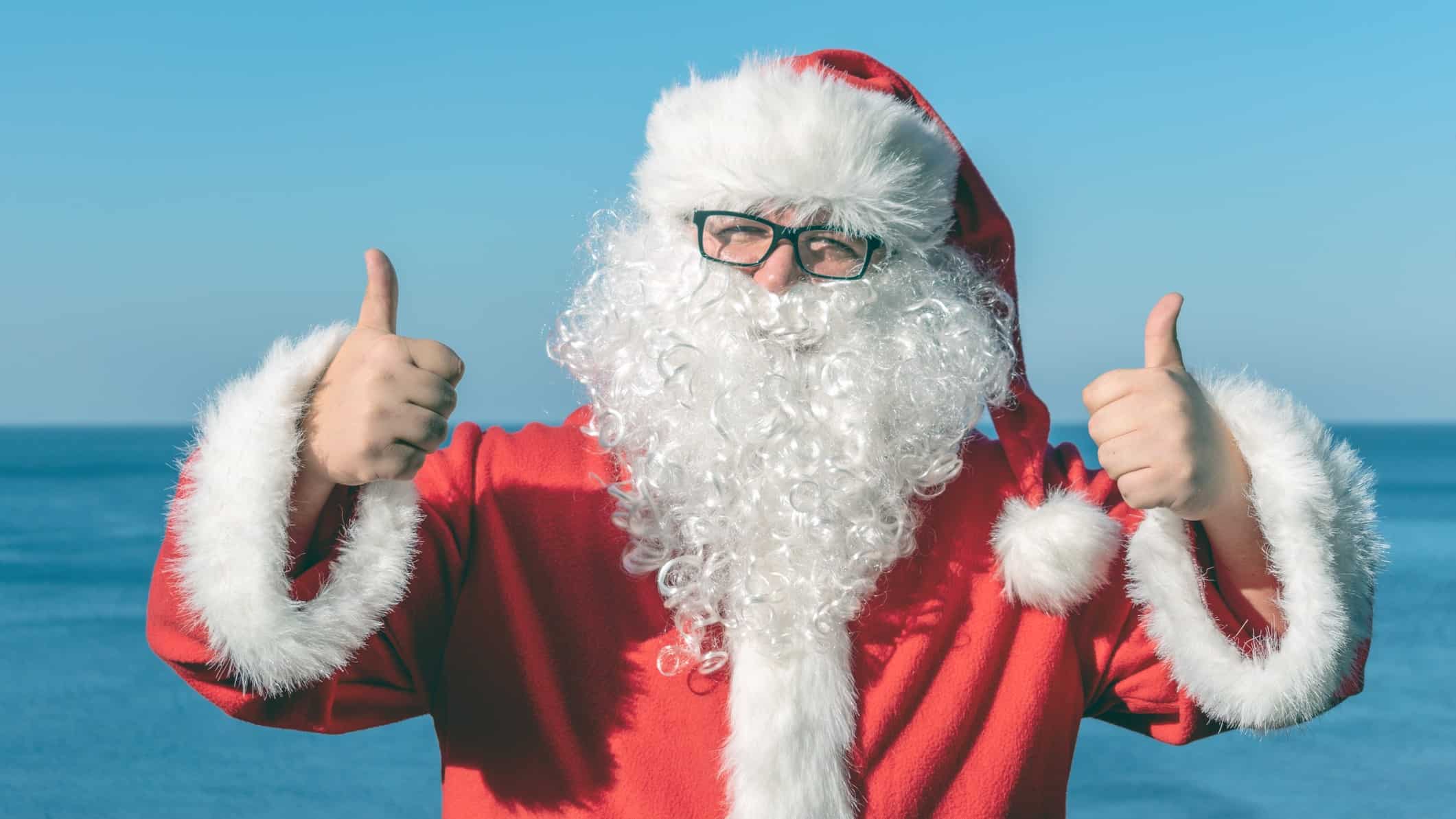 Santa at the beach gives a big thumbs up, indicating positive sentiment for the year ahead for ASX share prices