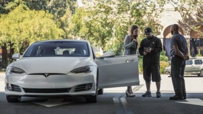 tesla stock represented by two people standing next to tesla electric vehicle