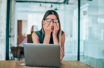 Investor covering eyes in front of laptop