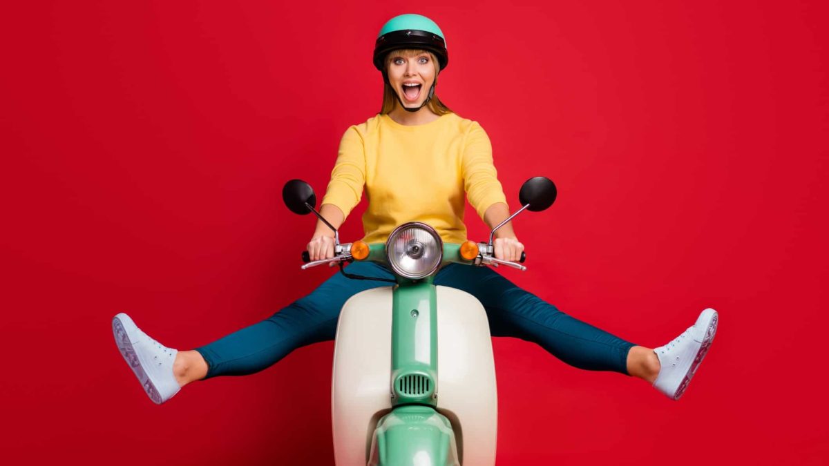Excited woman on scooter wearing helmet in front of red background