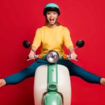 Excited woman on scooter wearing helmet in front of red background