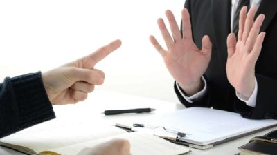 Two buisnessmen: one poining a finger, the other holding his hands up in denial