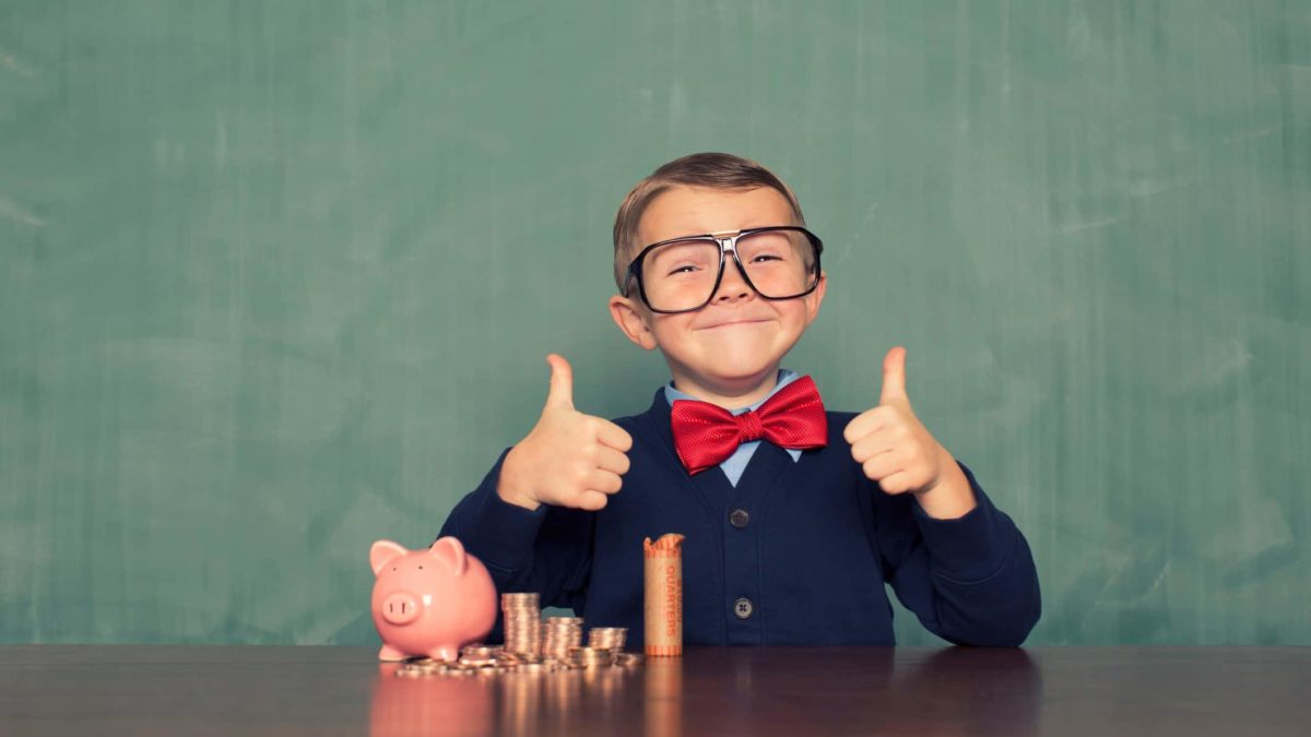 ASX bank shares buy A young boy in a business suit giving thumbs up with piggy banks and coin piles
