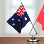 Two flags - one from China, the other Australian - sit together on a desk