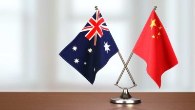Two flags - one from China, the other Australian - sit together on a desk