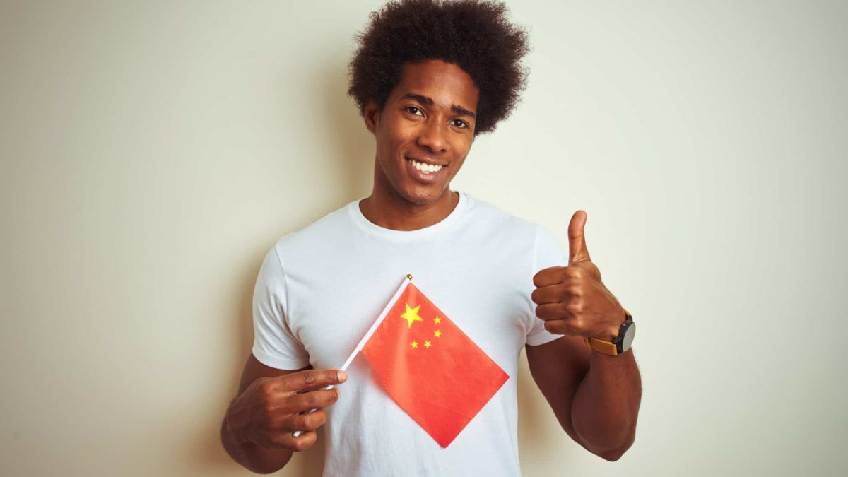 A man holds a Chinese flag and give the thumbs up, indicating approval for Chinese shares trading on US stock market