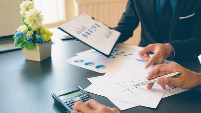 Two business workers at a desk comparing companies to analyse the best option for share price returns